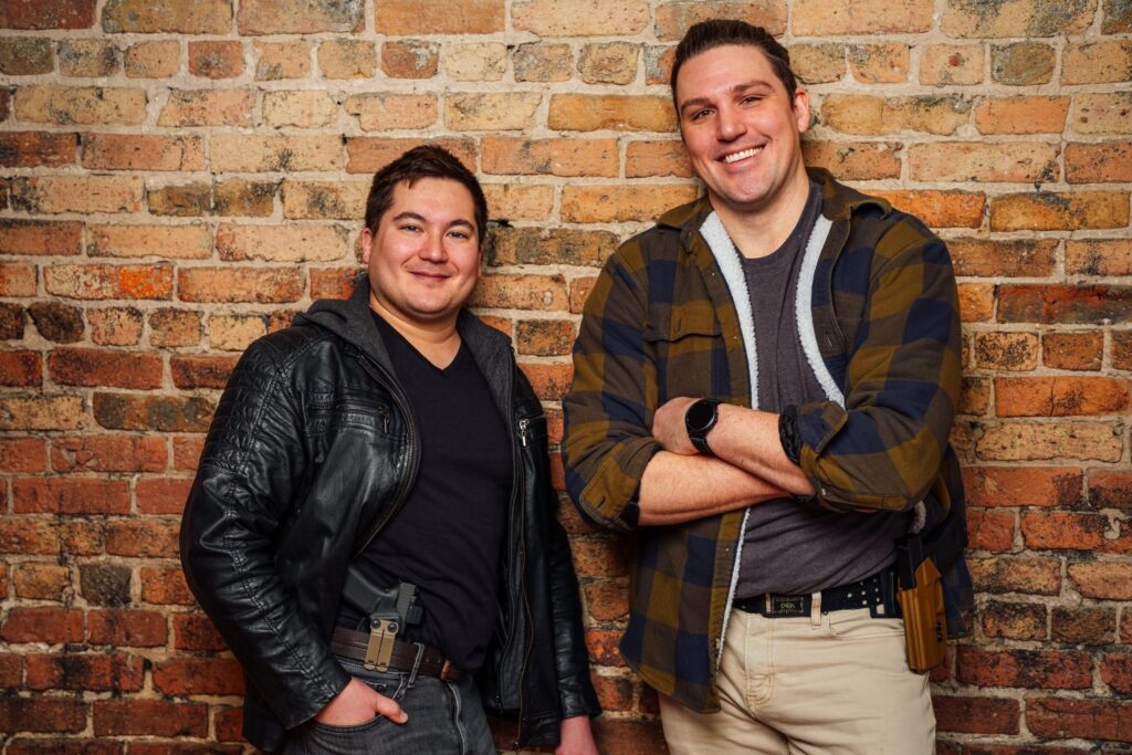 Two people standing in front of a brick wall, from Trigrd’s mission page.